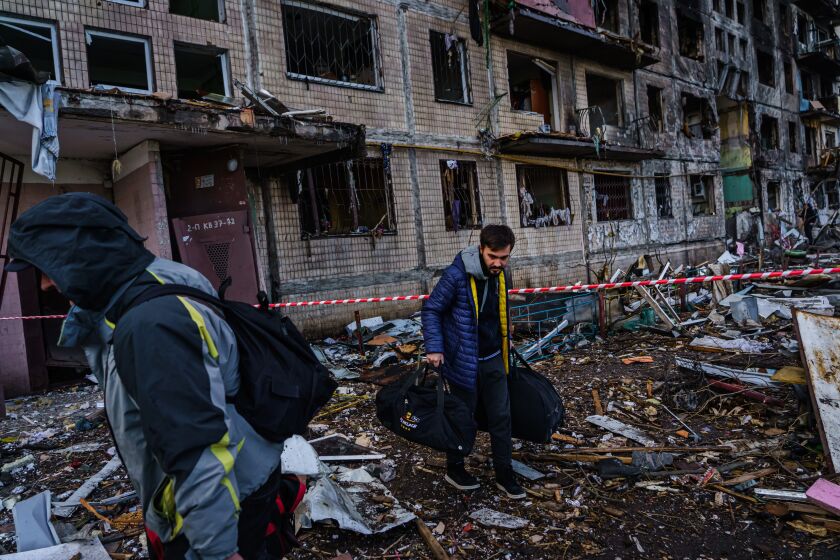 IRPIN, UKRAINE -- MARCH 14, 2022: Local residents carry bags out and get to safety after the apartment building behind them is damaged by what Kyiv officials call a Russian bombardment in the Obolon neighborhood of Irpin, Ukraine, Monday, March 14, 2022. (MARCUS YAM / LOS ANGELES TIMES)