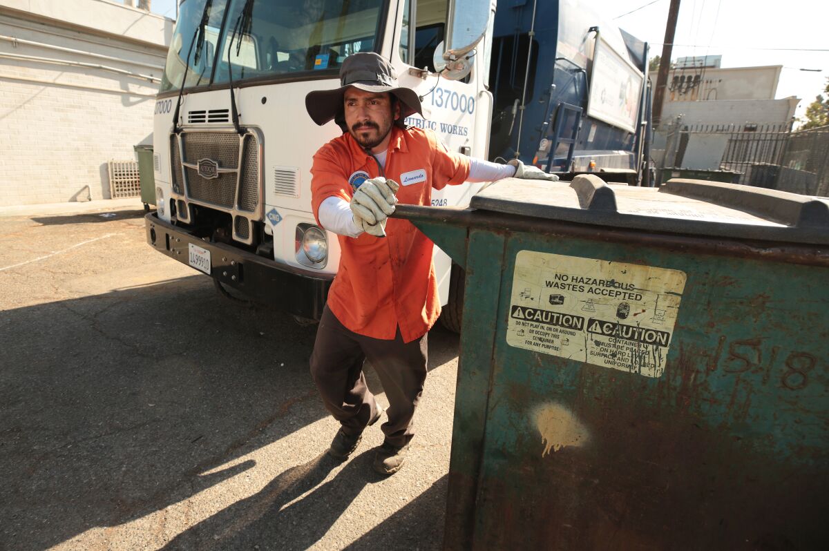 Leonardo Zamudio, a sanitation worker, loads a large trash bins into a sanitation truck.