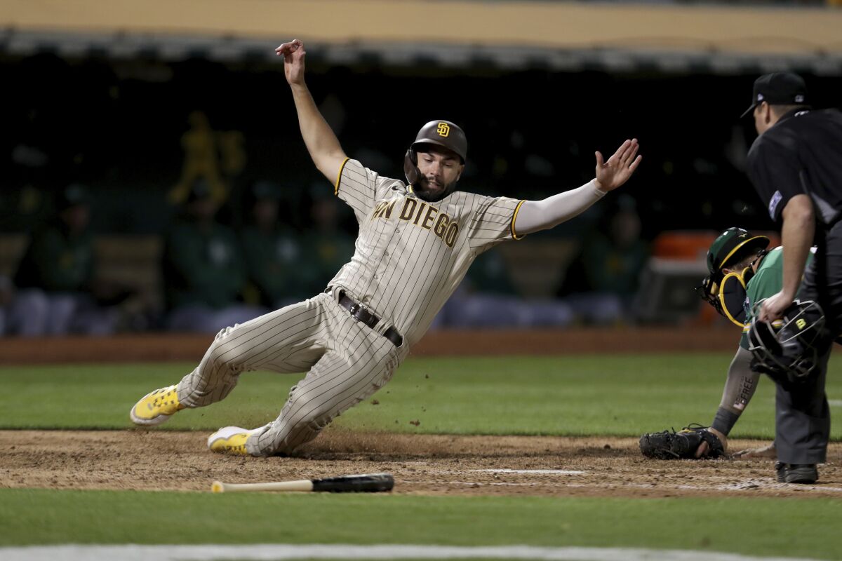 San Diego Padres' Eric Hosmer, left, scores on a single by Trent Grisham, in front of Oakland Athletics catcher Yan Gomes, right, during the seventh inning of a baseball game in Oakland, Calif., Tuesday, Aug. 3, 2021. (AP Photo/Jed Jacobsohn)