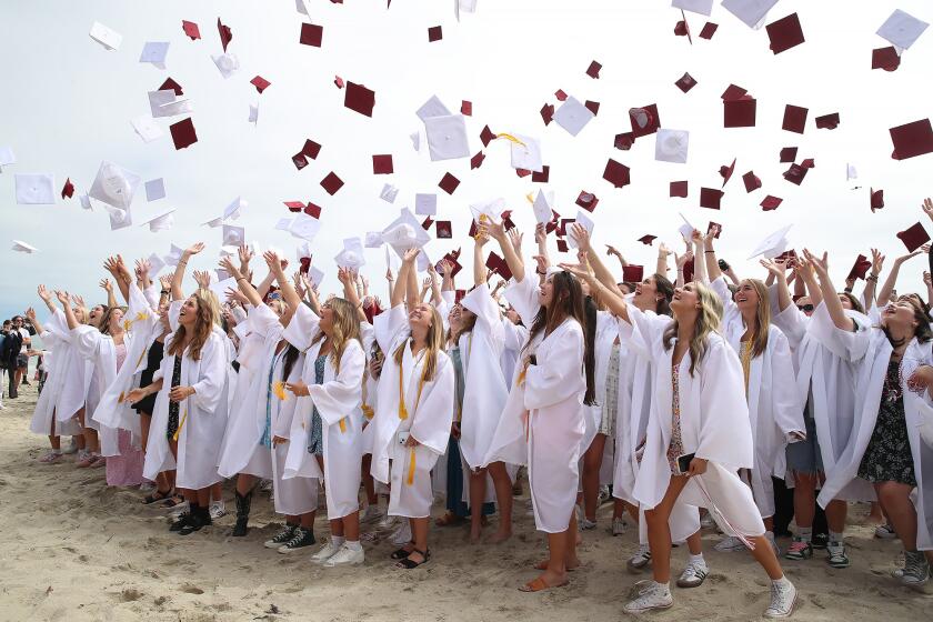 Graduates throw their caps into the air as they celebrate traditional celebratory "grad-walk" finale at Main Beach Park on Wednesday in downtown Laguna Beach.