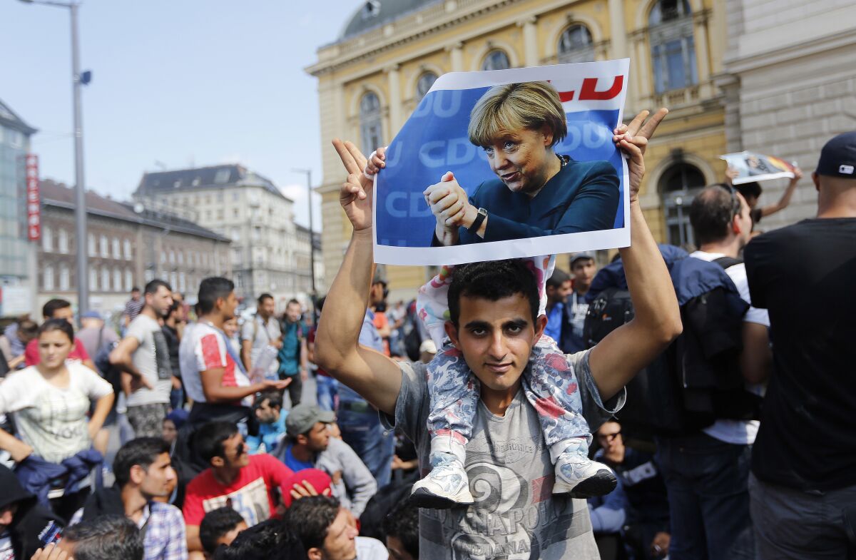 FILE - A migrant holds up a poster of German Chancellor Angela Merkel before starting a march out of Budapest, Hungary, towards Austria and Germany, Sept. 4, 2015. Merkel became the face of a welcoming approach to migrants as people fleeing conflicts in Syria and elsewhere trekked across the Balkans. More than 1 million asylum-seekers entered Germany in 2015-16. (AP Photo/Frank Augstein, file)