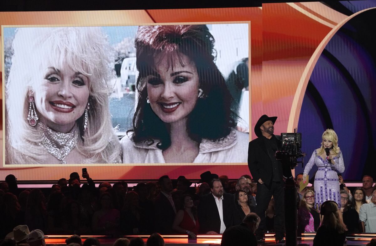 Garth Brooks and Dolly Parton appear in front of a screen showing a photo of Naomi Judd and Parton