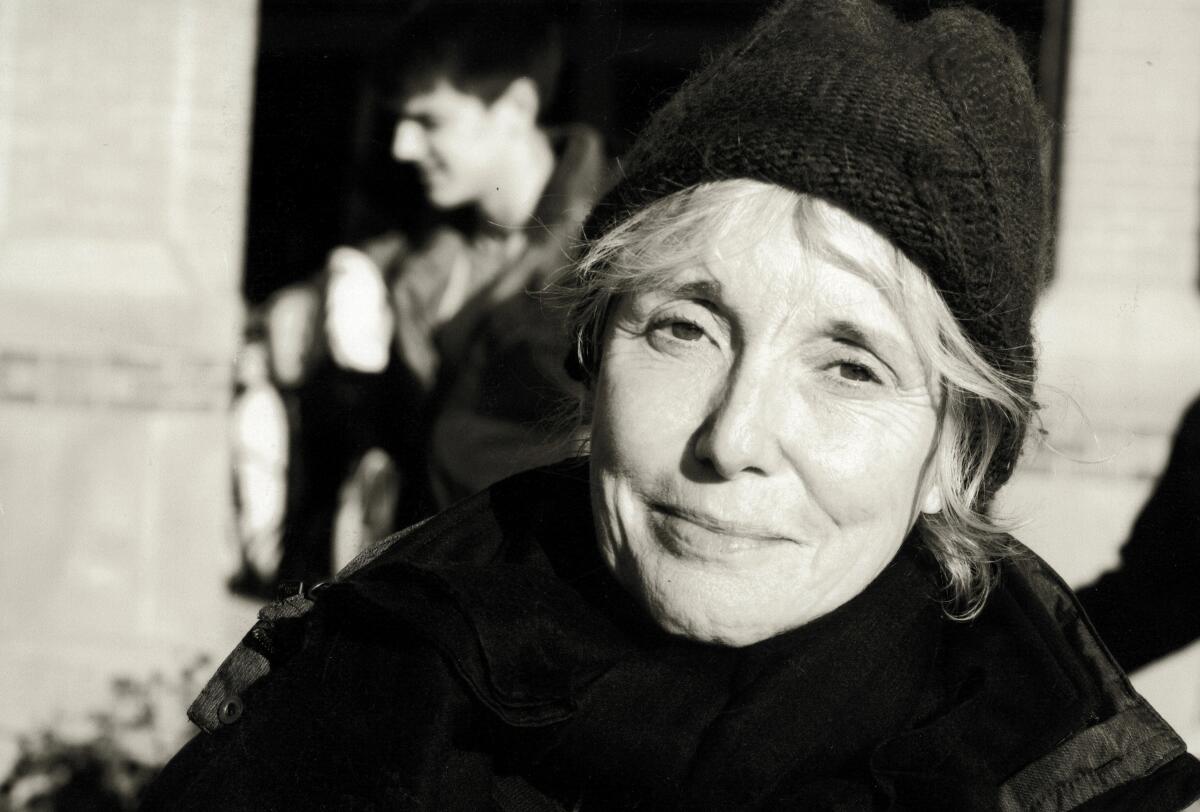 A black-and-white photo of a smiling woman in a knit cap and jacket.