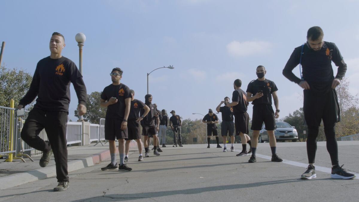 Two lines of men in all-black workout clothing in a parking lot