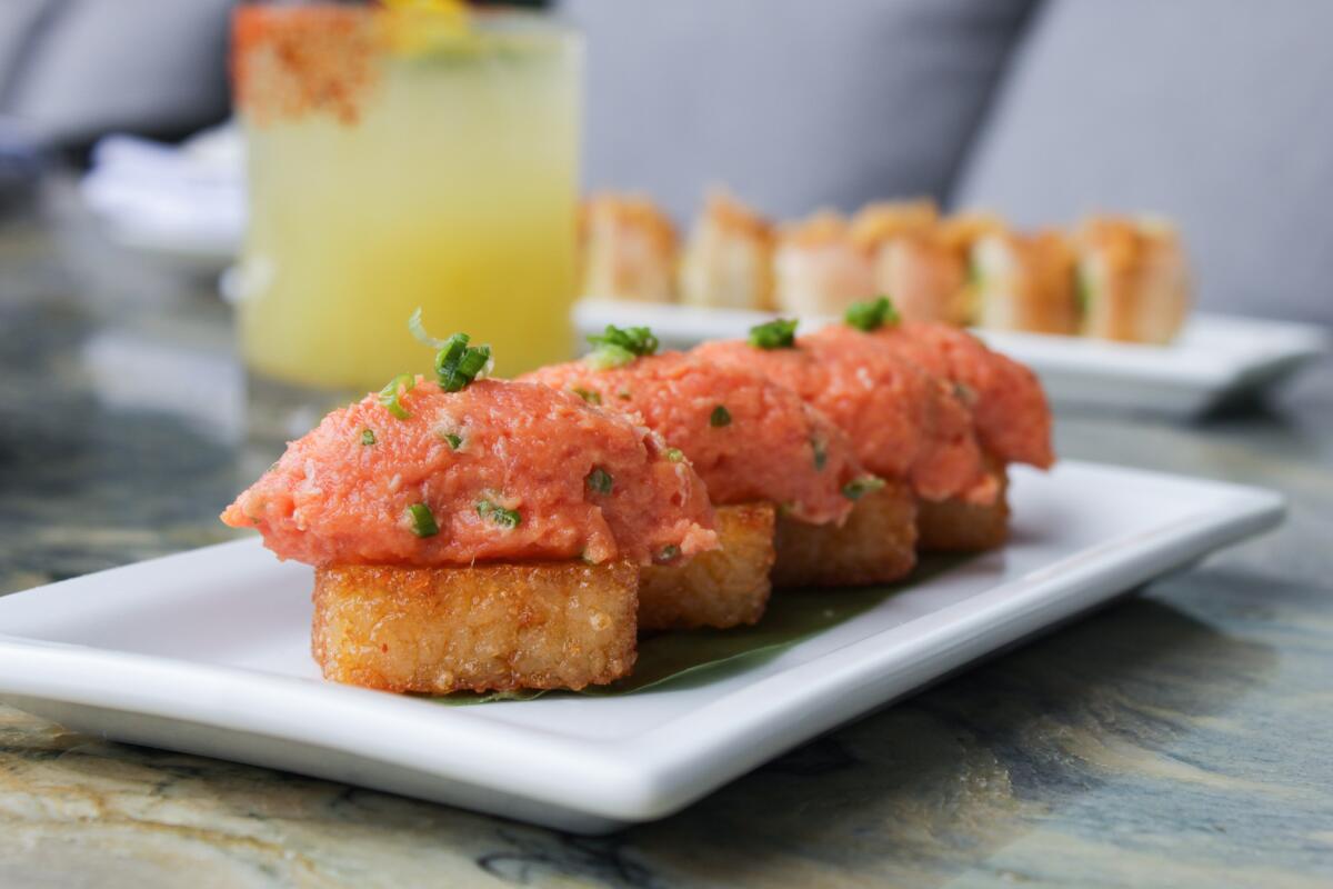 A closeup photo of Sushi Roku's spicy tuna on crispy rice. In the background is sushi and a cocktail.