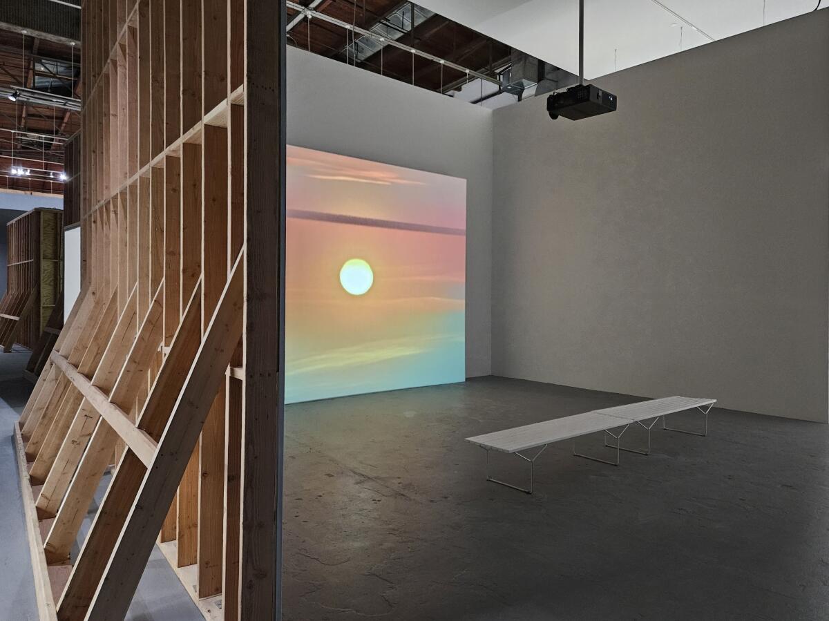 A sun surround by pink and blue hues projected on a screen inside a museum gallery.