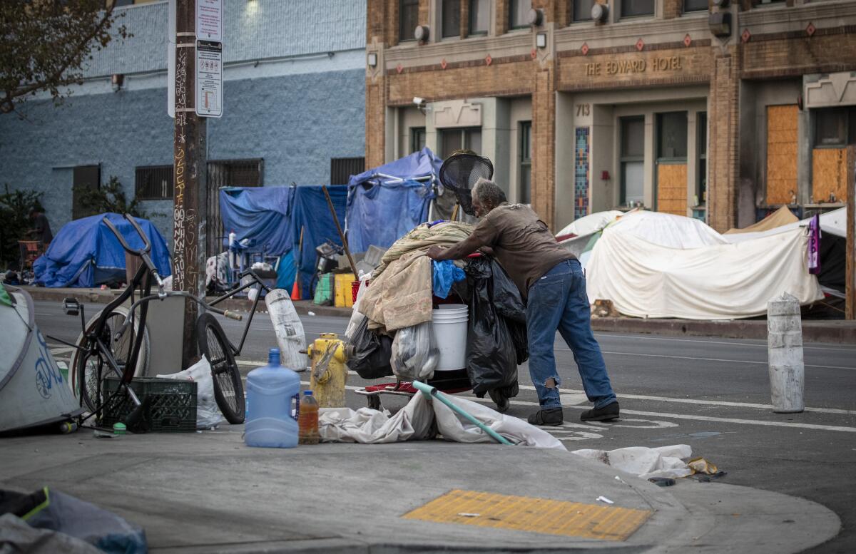 A person pushes a cart of their belongings through a homeless encampment on skid row in 2021.