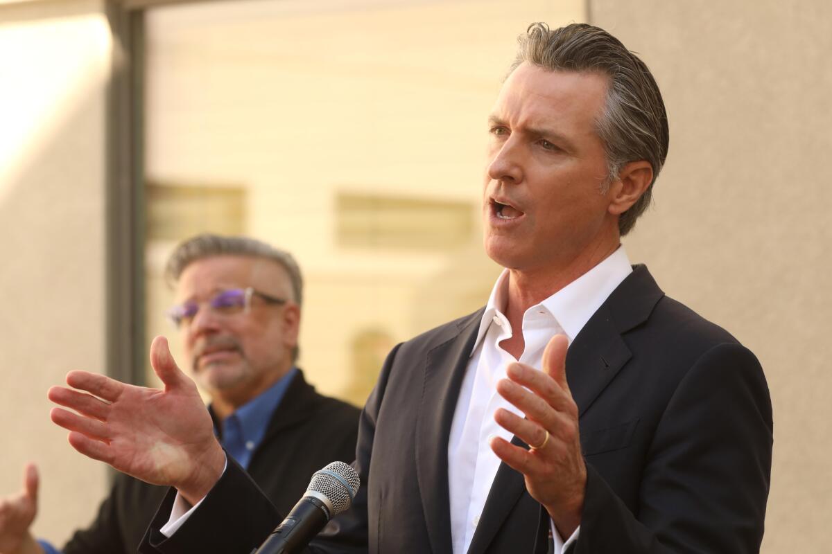 A man at a podium speaks and holds his hands up 