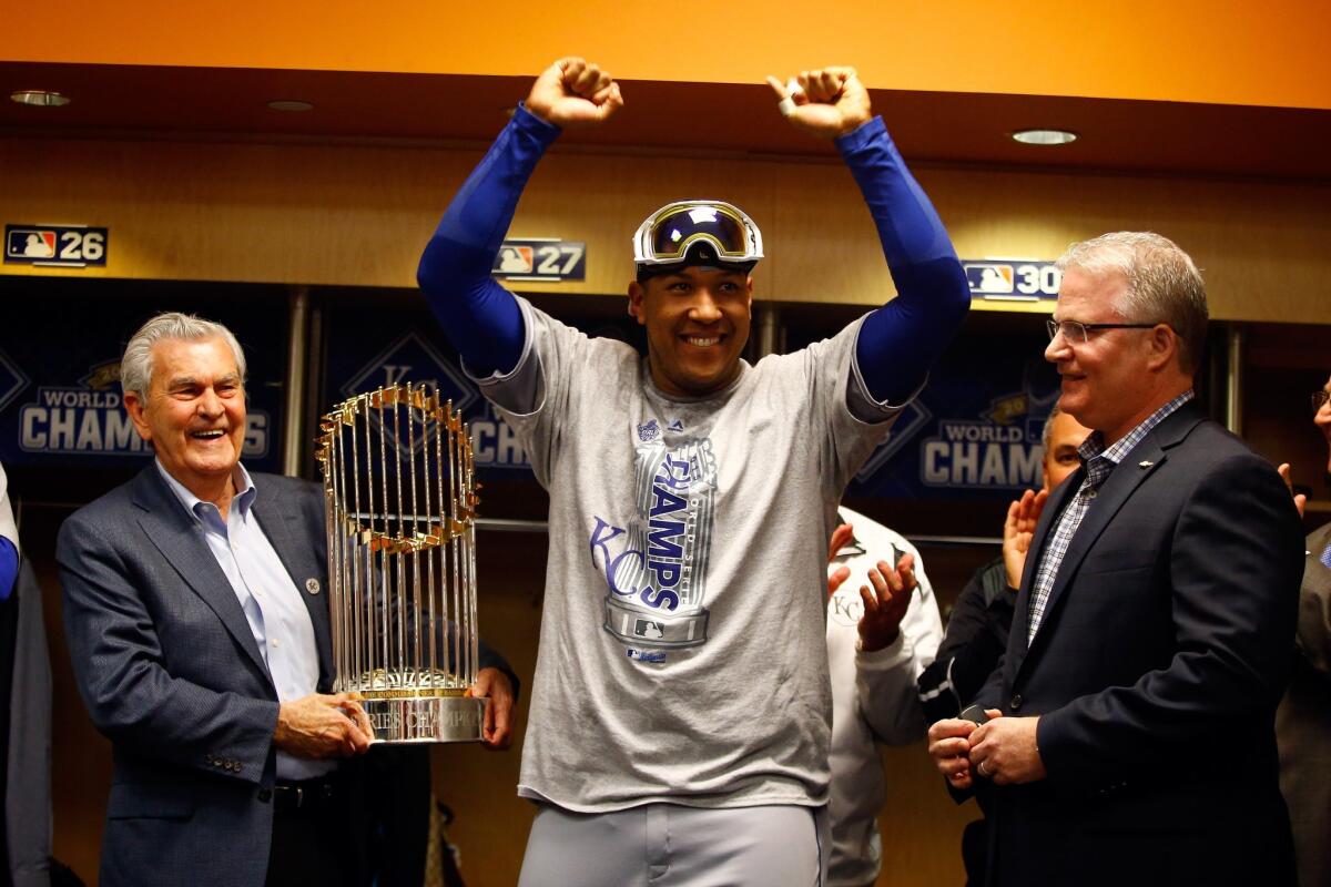 Salvador Perez of the Kansas City Royals celebrates in the clubhouse as Royals owner David D. Glass, left, holds the Commissioner's Trophy after the Royals beat the New York Mets to win Game 5 of the 2015 World Series.