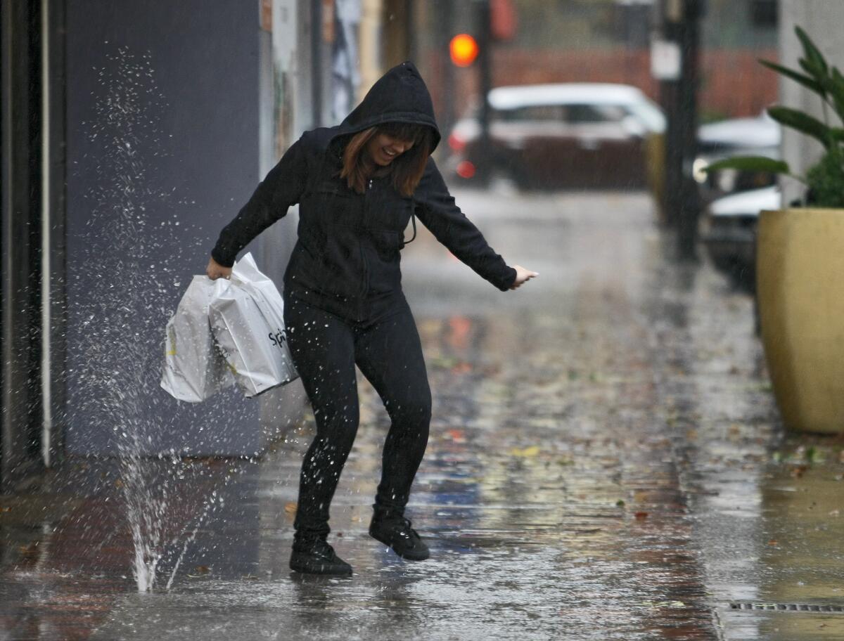 A woman tries to avoid the rain and water popping up from a drain on San Fernando Blvd. near Magnolia Blvd. in Burbank on Friday, Feb. 28, 2014. Rain is predicted through the weekend.