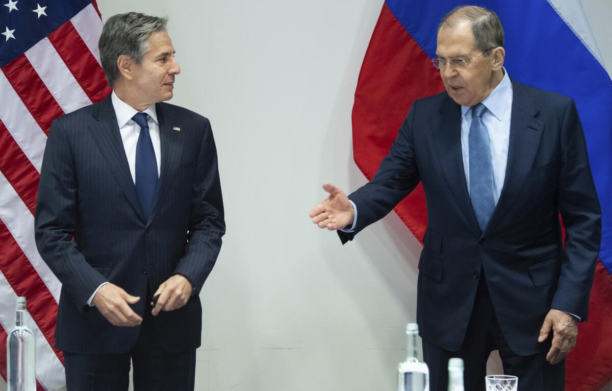 Two men in suits stand before flags.