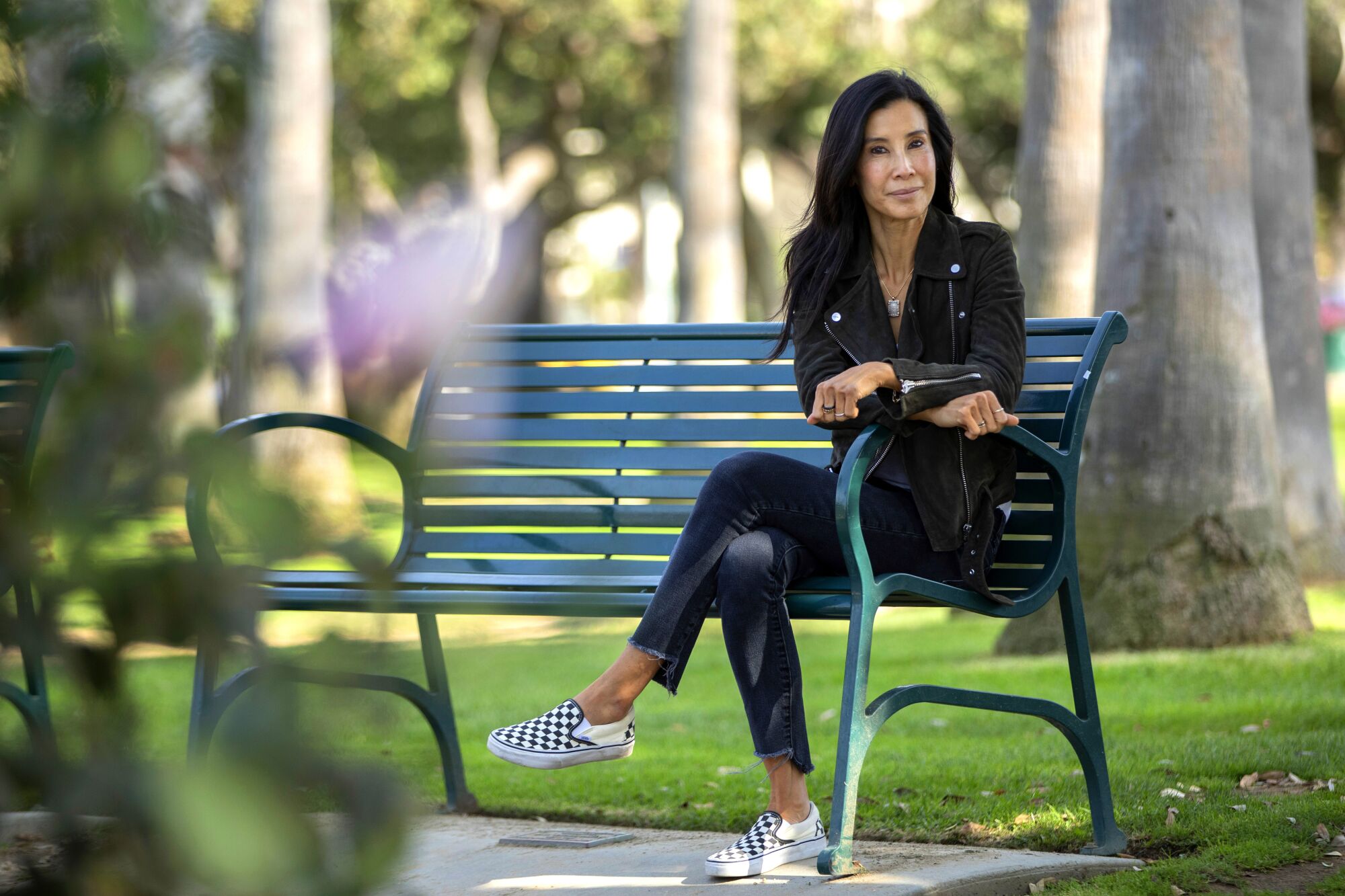 Journalist Lisa Ling sits on a bench in a park.