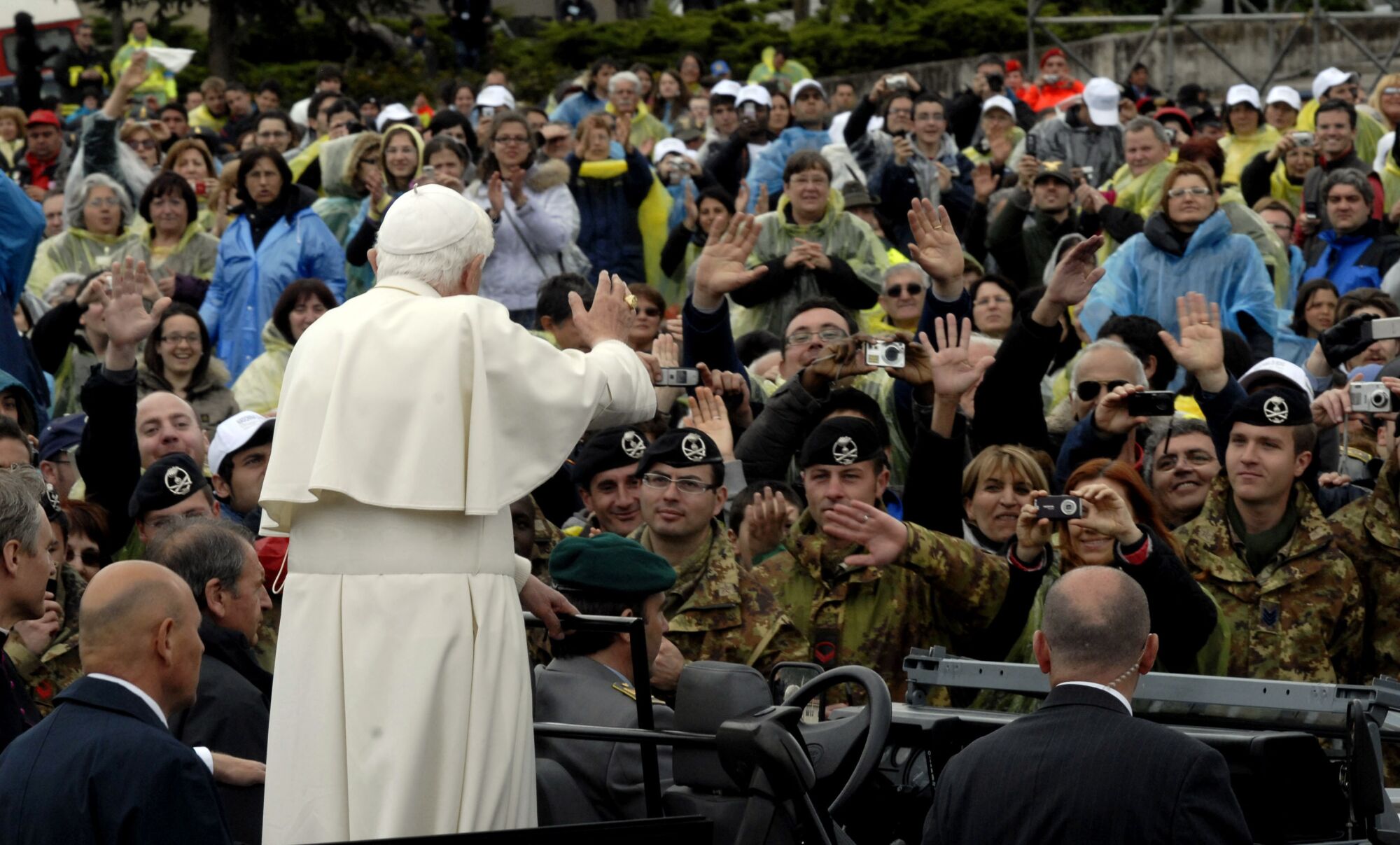 Papa Benedict XVI, bir grup askeri kalabalığa dahil eden insanlara el sallıyor.