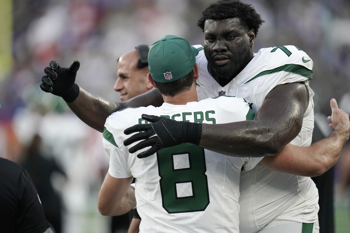 New York Jets offensive tackle Mekhi Bectonhugs quarterback Aaron Rodgers (8) during a preseason game.