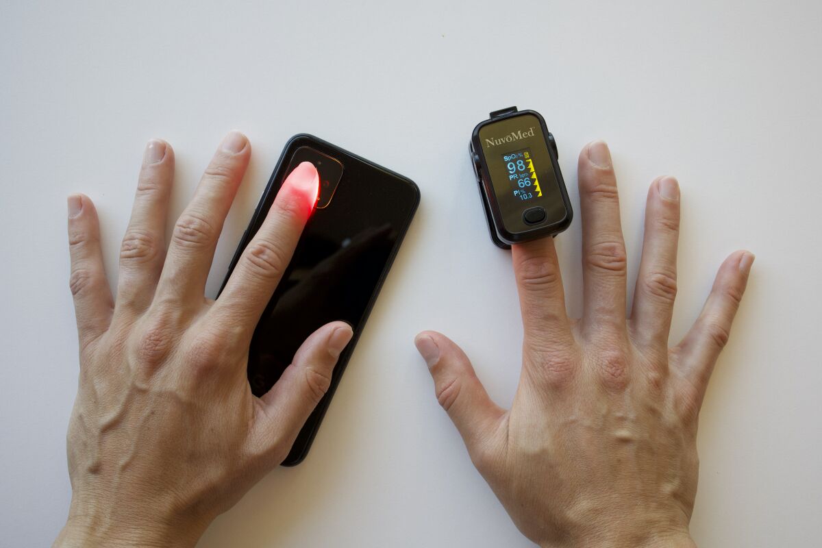 A participant simultaneously tests the new smartphone oximetry technique (left) and a standard pulse oximeter (right).
