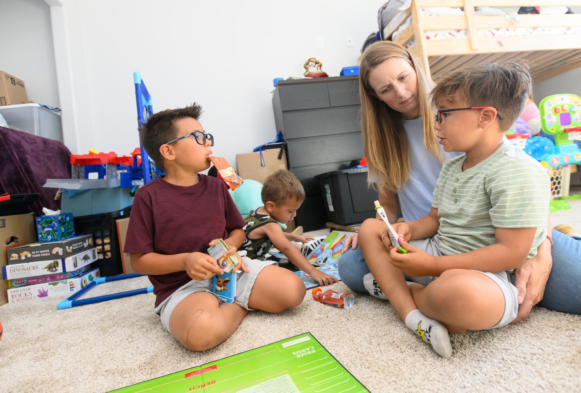 A mother plays with her young children on the floor. 