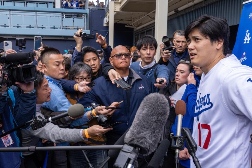Dodger Shohei Ohtani is surrounded by media cameras and microphones during DodgerFest 2024 Saturday