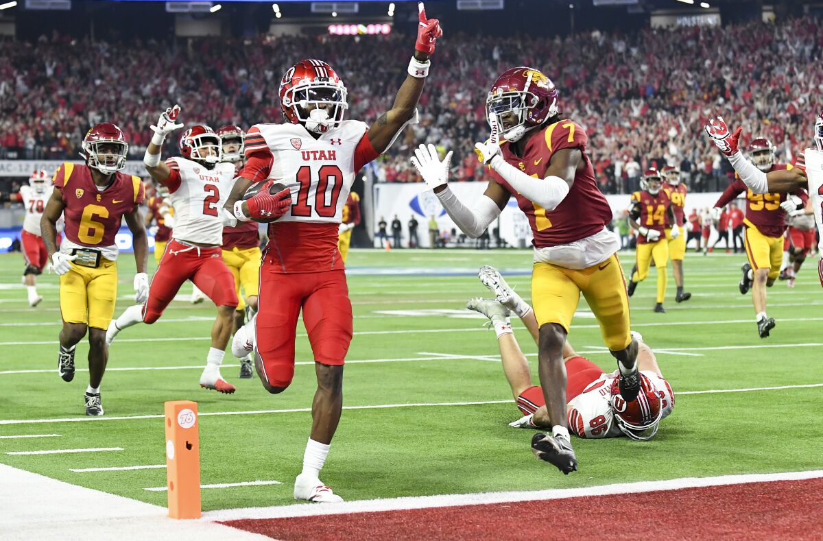 Utah receiver Money Parks holds up an index finger as he scores a touchdown in front of USC defensive back Calen Bullock.