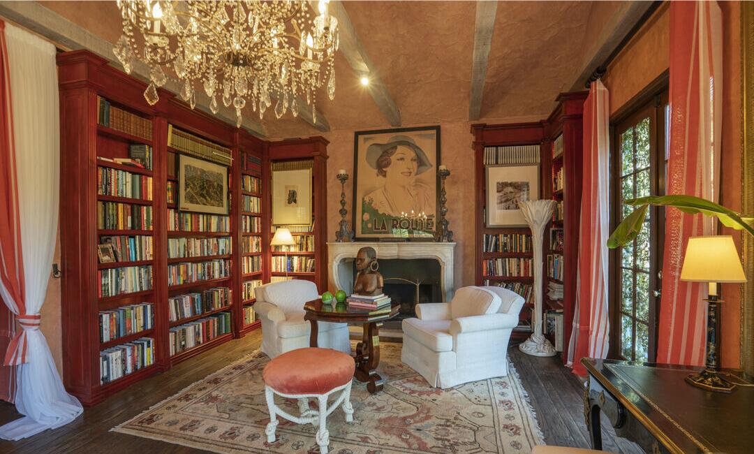 The library has tall bookshelves, a fireplace, seating and a window.