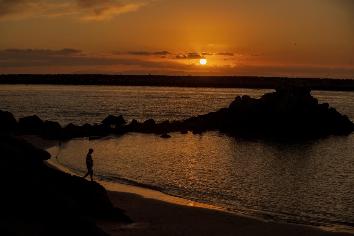 A beachgoer is silhouetted by a scenic sunset at Corona del Mar State Beach on Jan. 8, 2020. Warm weather is on tap for Southern California this weekend.