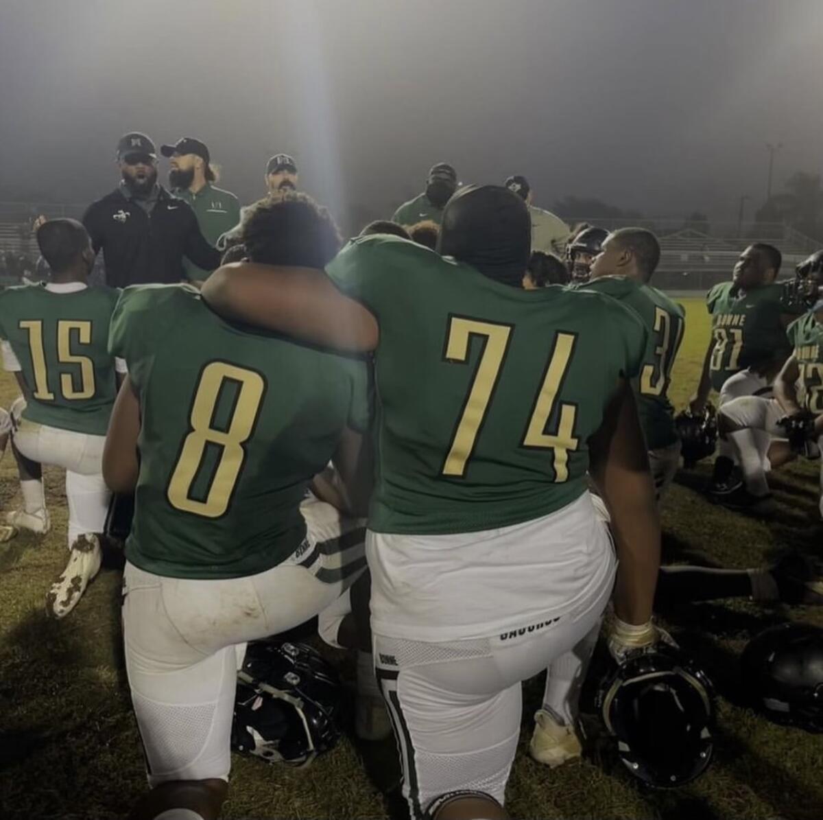 Narbonne players take a knee with their backs to the camera.