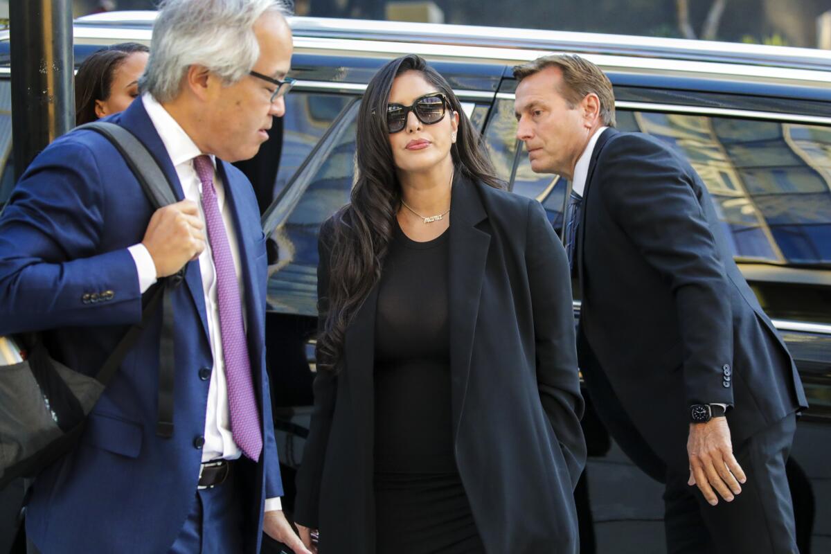 Vanessa Bryant dressed in black stands between two men in front of a vehicle.