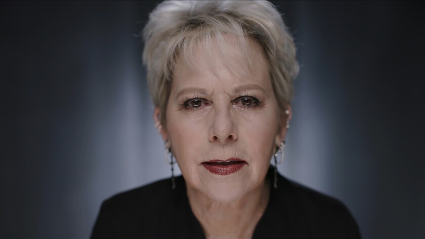 A woman with short grey hair stares into a camera