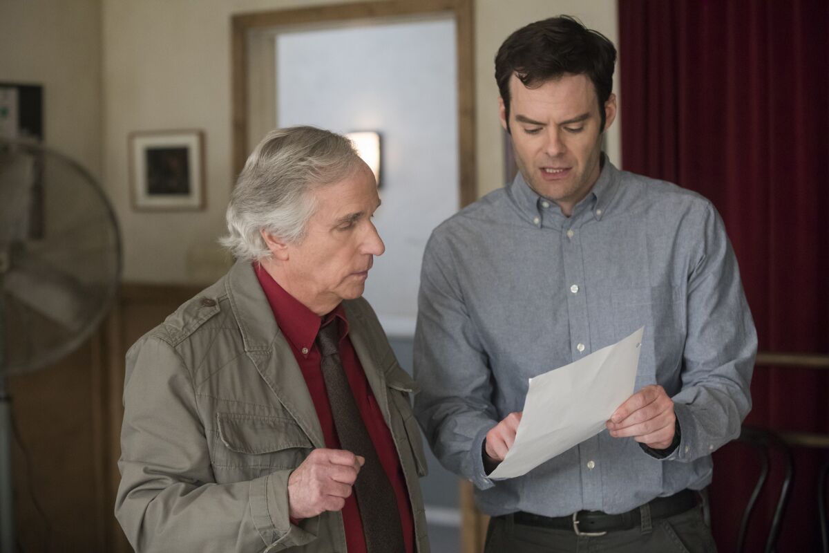 An older man and a younger man standing while looking at a piece of paper.