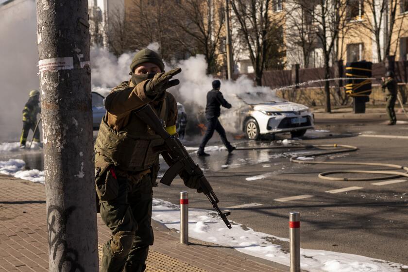 Ukrainian soldiers take positions outside a military facility as two cars burn, in a street in Kyiv, Ukraine, Saturday, Feb. 26, 2022. Russian troops stormed toward Ukraine's capital Saturday, and street fighting broke out as city officials urged residents to take shelter. (AP Photo/Emilio Morenatti)