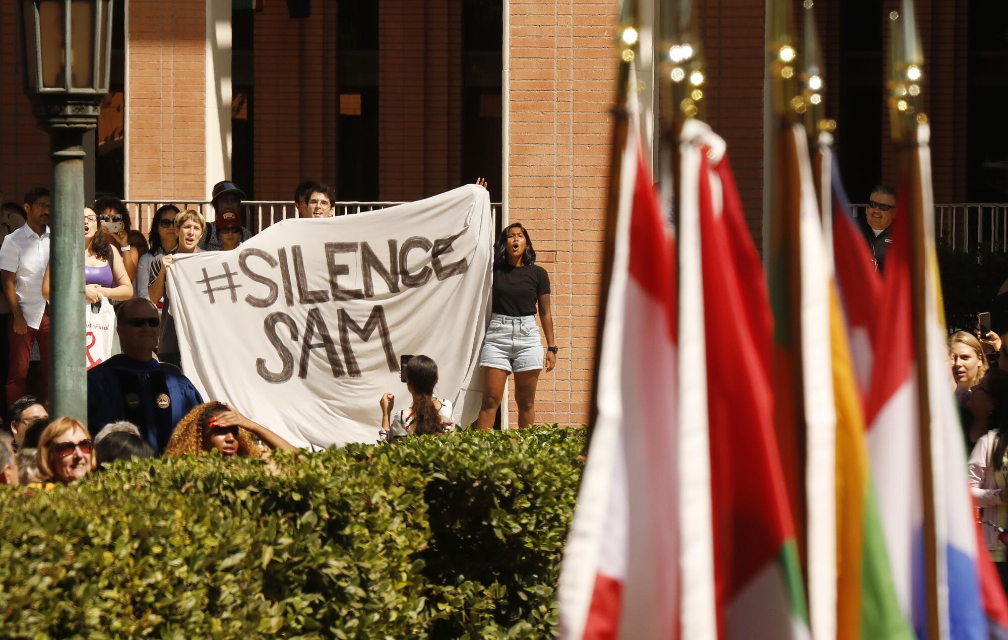 Protesters hold a banner reading "#Silence Sam."