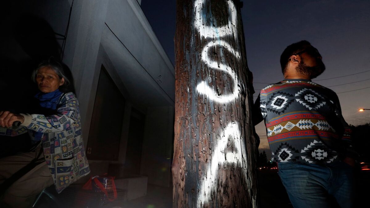 Seth Hernandez, 24, right, stands next to a pole spray painted with "USA" on it in Culver City on Dec. 7. Hernandez is a member of the sizable Asian community in Los Angeles that is undocumented.