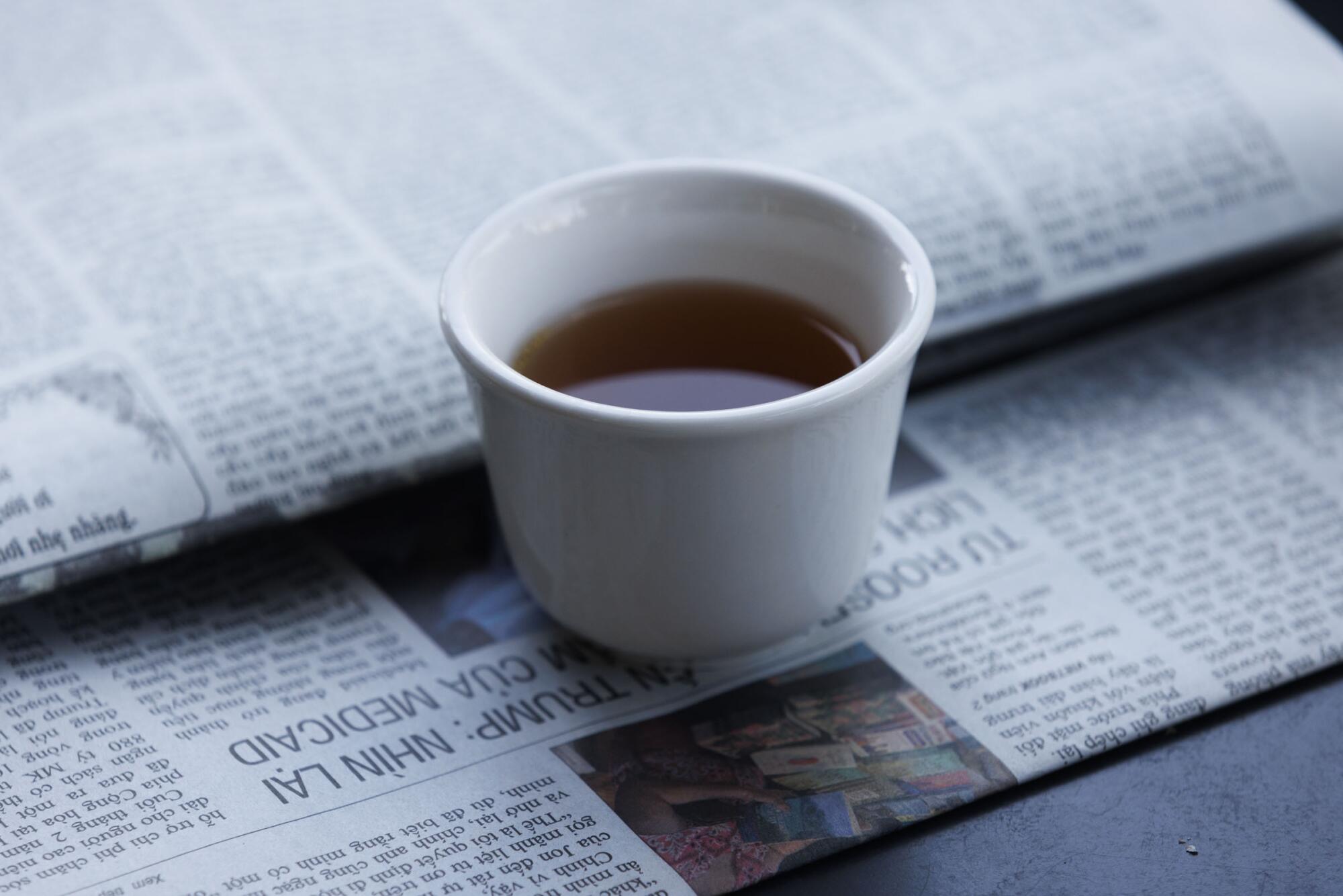 Una taza de té descansa sobre un periódico vietnamita en Coffee Factory.