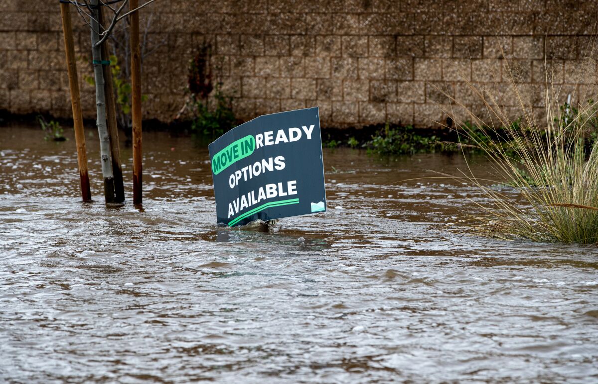 Floodwaters fill a street, covering part of a sign that reads "Ready to move in options available"