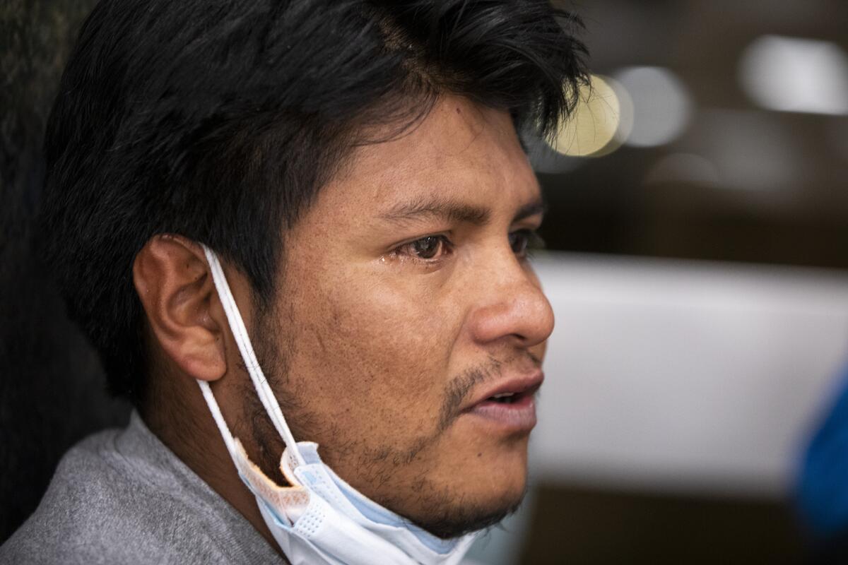 A closeup of a man with a tear escaping his eye as he speaks, his protective mask pulled under his chin