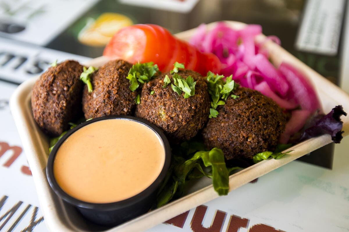 Freshly made falafel on a rectangular tray with orange sauce and sliced tomato and pickled turnip