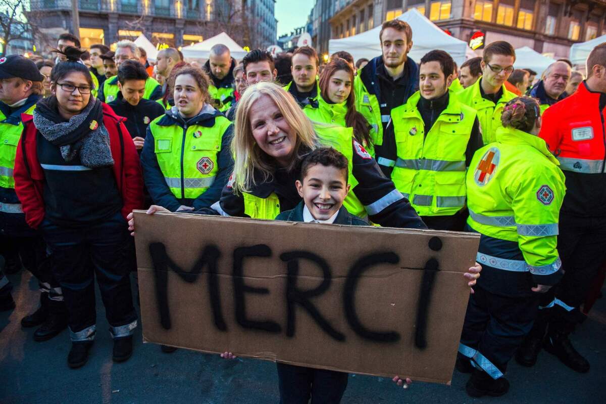 Emergency workers posing with a boy holding a placard reading "thank you", as people gather to pay tribute to the victims of the Brussels terror attacks.