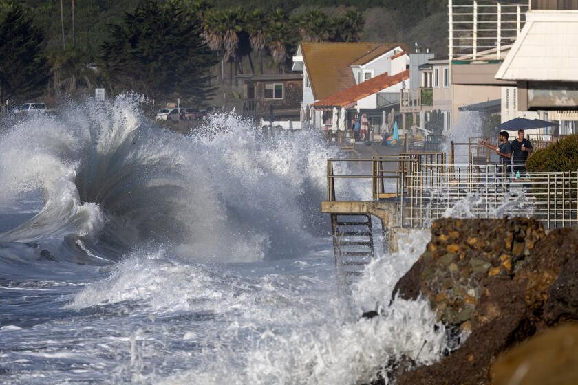 Ventura, CA - December 28: Men watch from a balcony in Faria Beach as huge waves crash on the shore Thursday, Dec. 28, 2023 in Ventura, CA. (Brian van der Brug / Los Angeles Times)