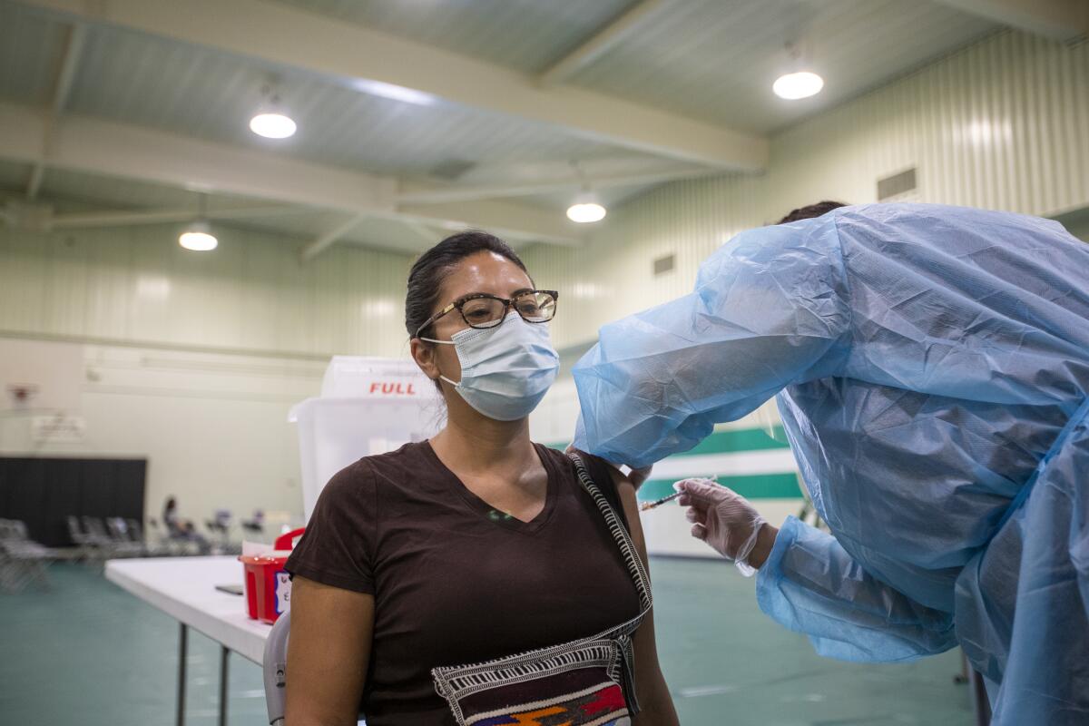 A nurse gives a vaccine shot to a teacher inside a school gym.