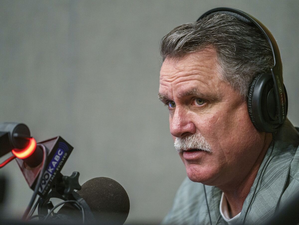 A man with a mustache wears headphones in front of a radio microphone