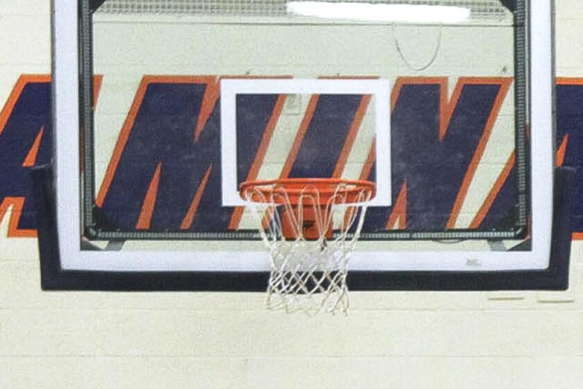 A basketball hoop and glass backboard, with the word "Chaminade" on a wall in the background