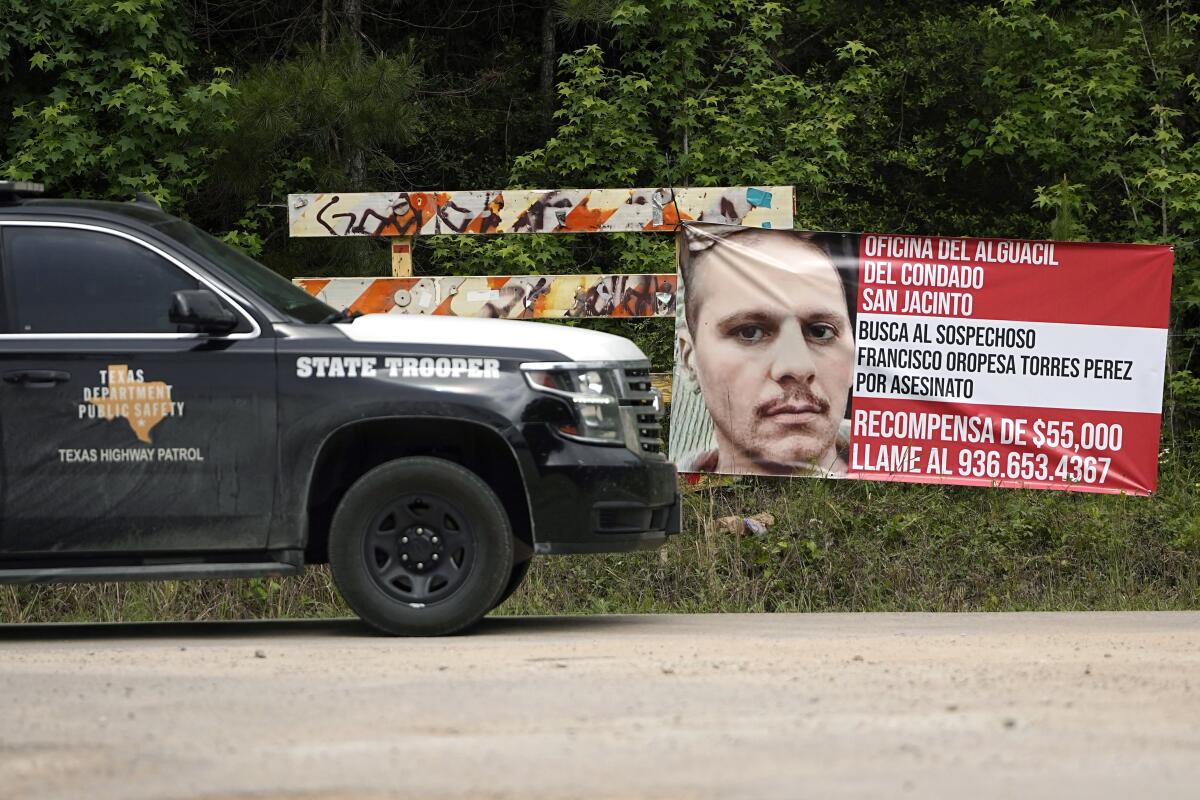 A Texas state trooper vehicle passes a posted wanted sign for a mass shooting suspect 