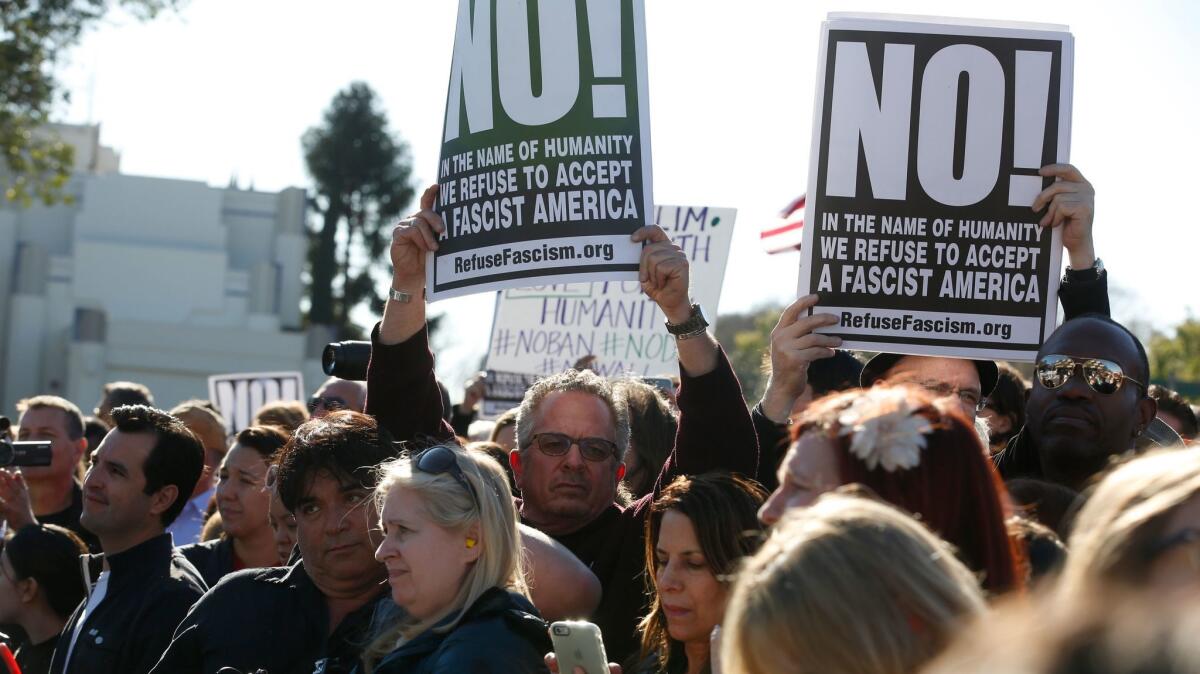 Keith James, center, of RefuseFascism.Org, holds up a sign during the United Voices rally outside United Talent Agency headquarters.
