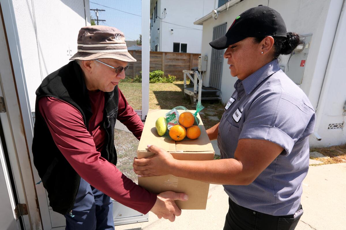 David Greenwald receives a box of food from Esthela Lopez, with Revolution Foods, at his home in Los Angeles. 