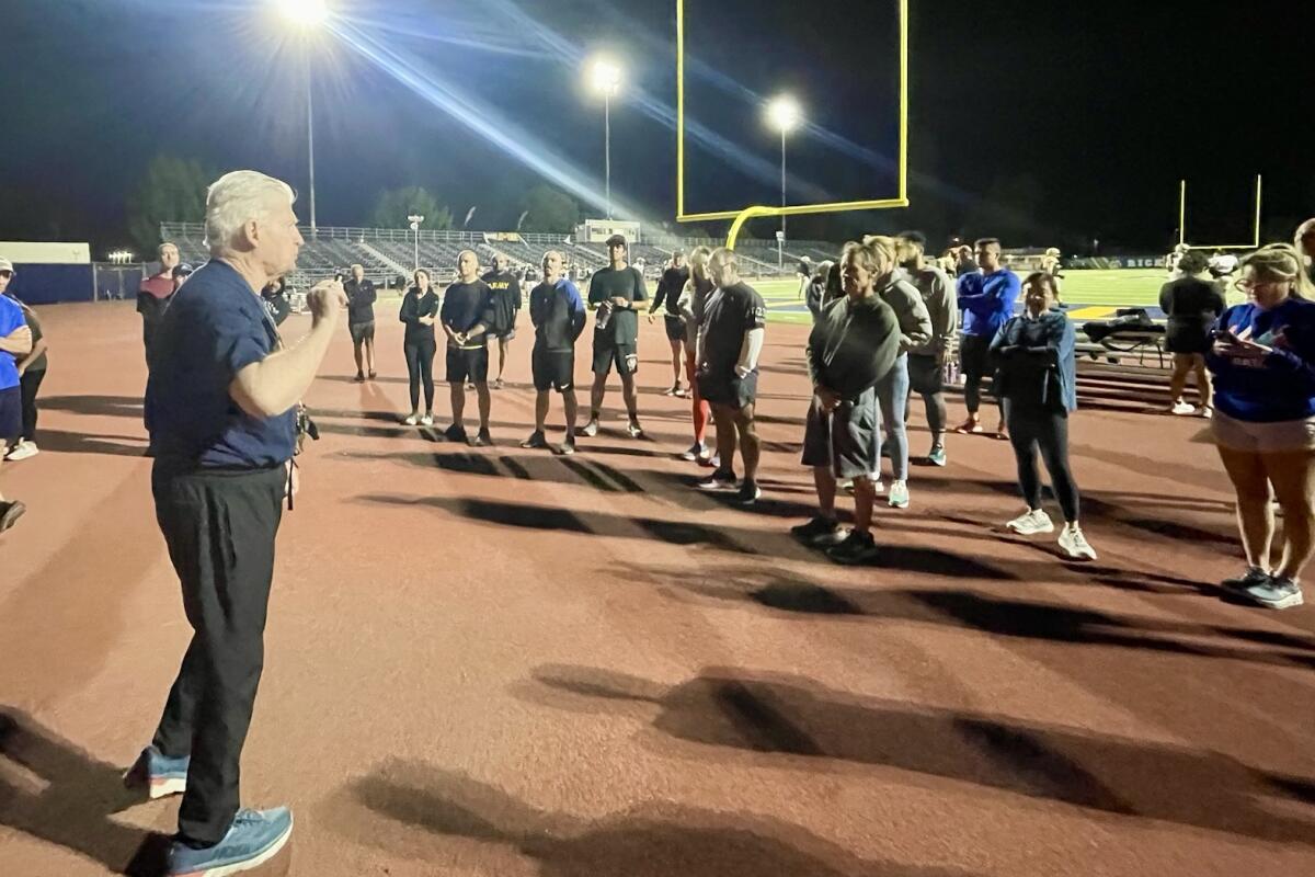 A gray-haired man addresses a group of runners on a high school football field