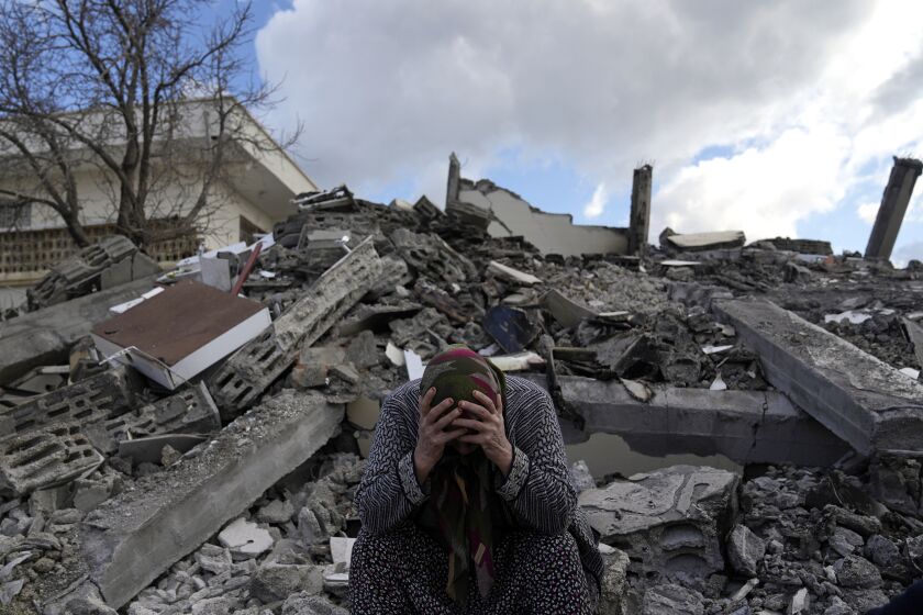 A woman sits on the rubble as emergency rescue teams search for people under the remains of destroyed buildings in Nurdagi town on the outskirts of Osmaniye city southern Turkey, Tuesday, Feb. 7, 2023. A powerful earthquake hit southeast Turkey and Syria early Monday, toppling hundreds of buildings and killing and injuring thousands of people. (AP Photo/Khalil Hamra)