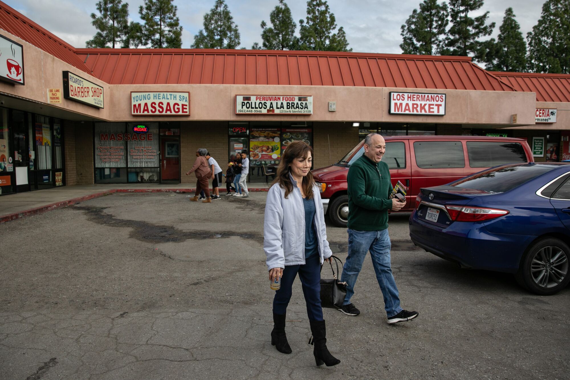 A couple walks near a restaurant in a strip mall.