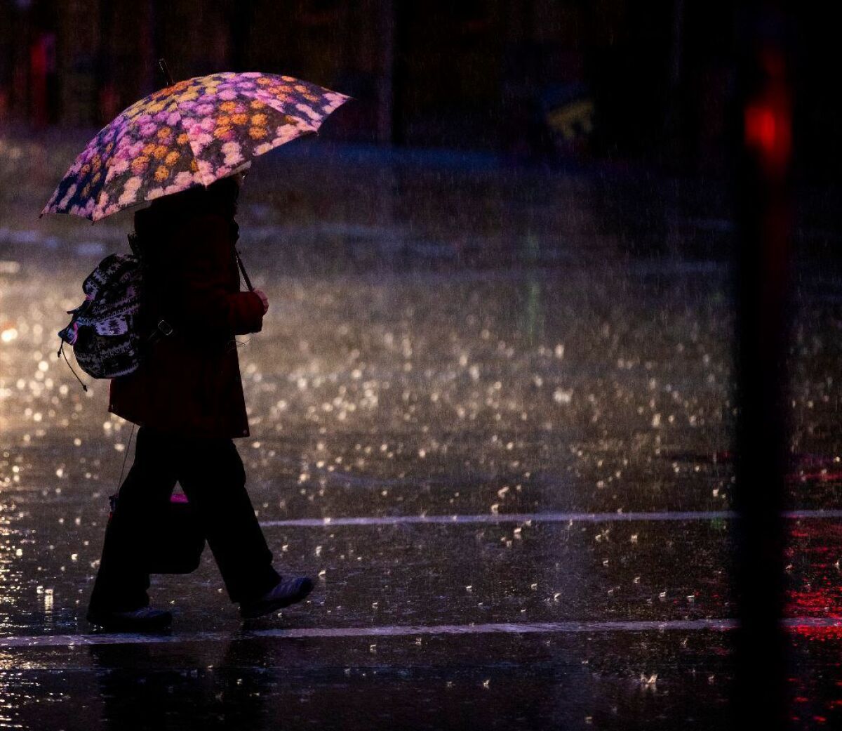 A pedestrian's umbrella is back lit by headlights, stop lights and street lights in the rain in Old Pasadena.
