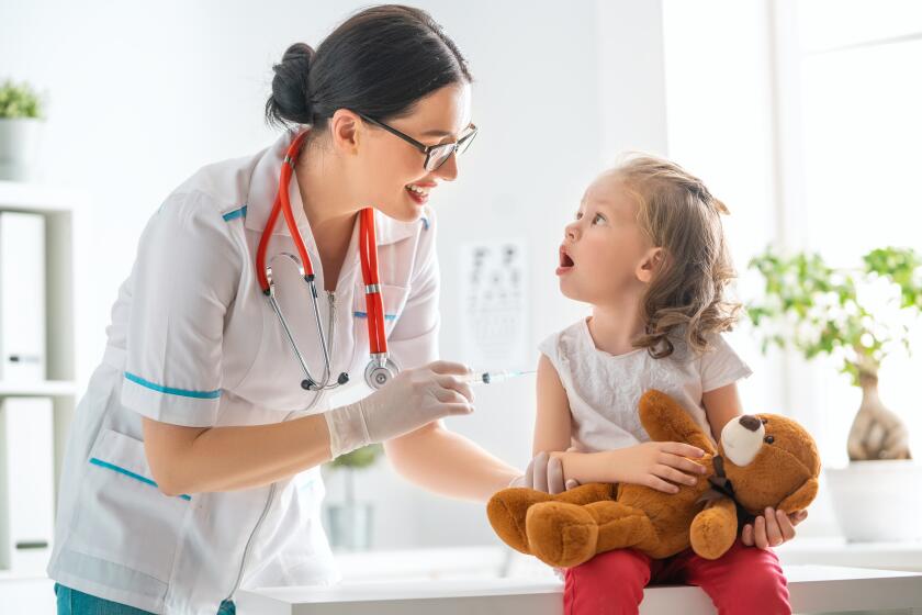 A doctor administers a vaccination to a child who is holding a teddy bear.