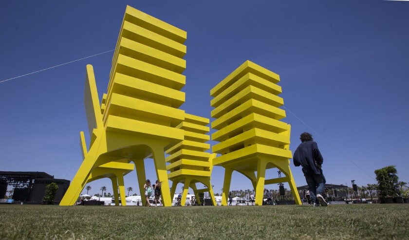 Several chair-like structures bearing towering buildings, all painted bright yellow, stand on a grassy lawn.