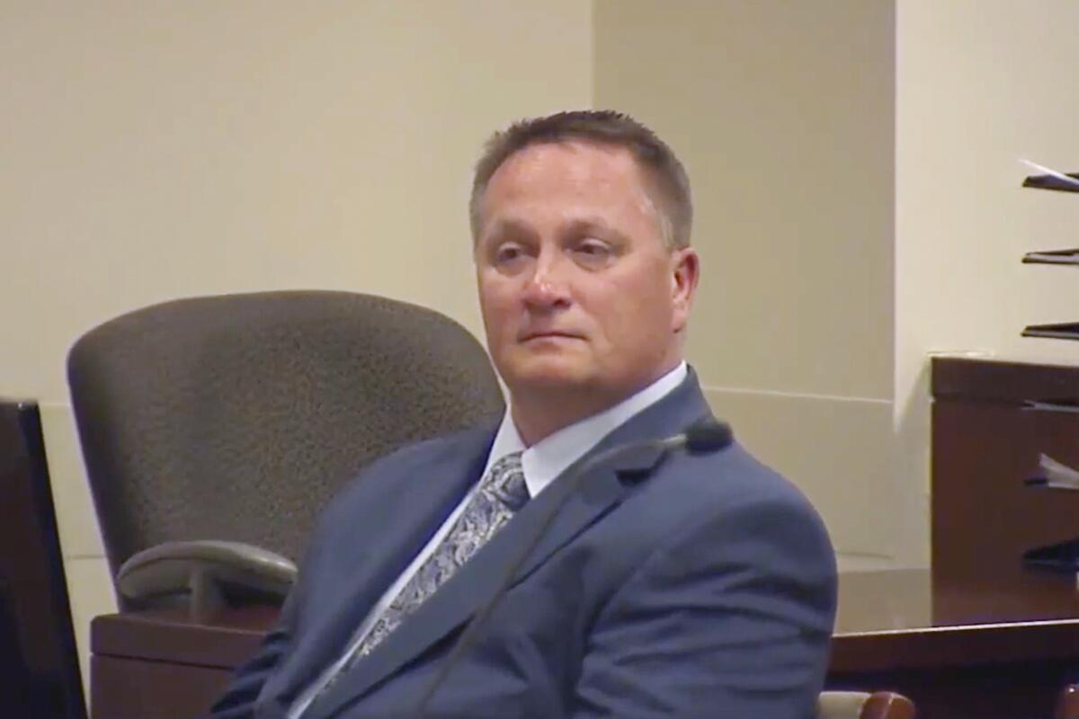 A man wearing a blue suit and tie sits in a courtroom.  